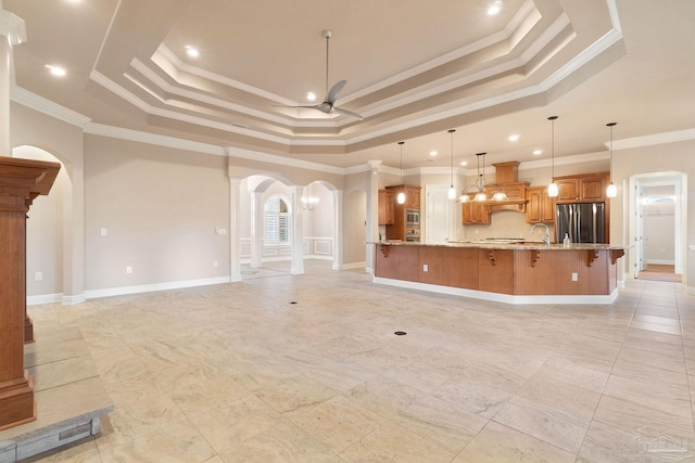 unfurnished living room featuring arched walkways, a ceiling fan, baseboards, a raised ceiling, and decorative columns