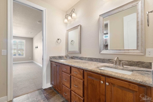 full bath featuring a sink, a textured ceiling, baseboards, and double vanity