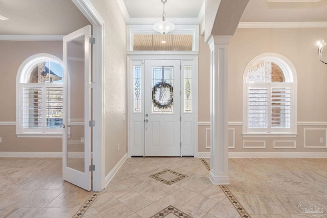 entrance foyer featuring baseboards, ornamental molding, a decorative wall, and ornate columns