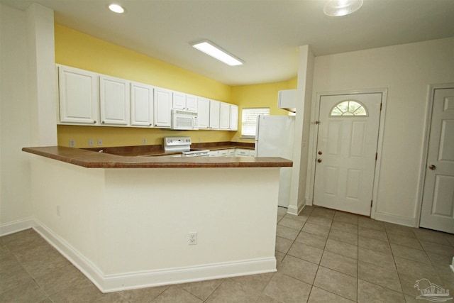 kitchen with light tile patterned flooring, kitchen peninsula, white appliances, and white cabinets