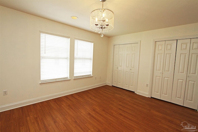 unfurnished bedroom with two closets, dark hardwood / wood-style floors, and a chandelier