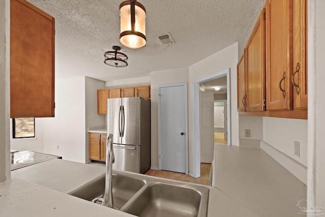 kitchen with pendant lighting, sink, a textured ceiling, and stainless steel fridge