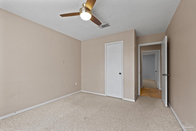 unfurnished bedroom featuring light colored carpet, a textured ceiling, and ceiling fan