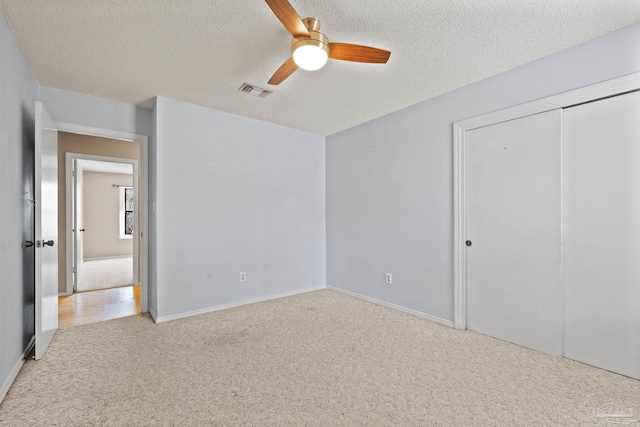 unfurnished bedroom featuring ceiling fan, a textured ceiling, a closet, and light carpet