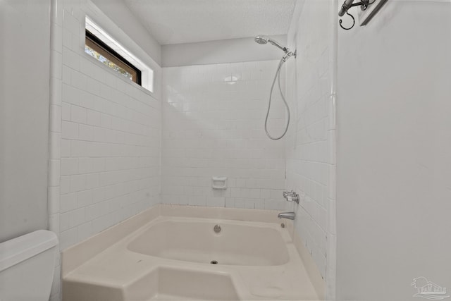 bathroom featuring a textured ceiling, toilet, and tiled shower / bath