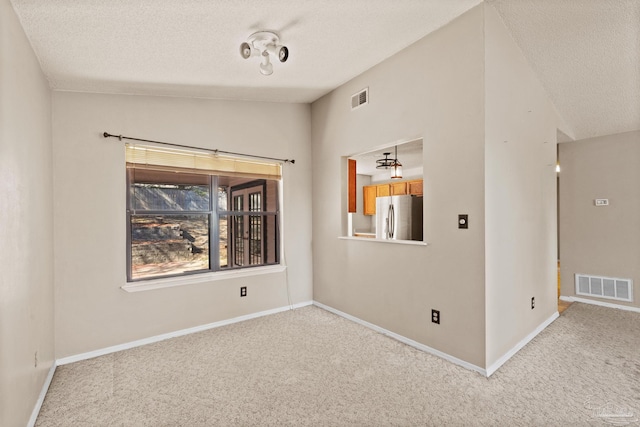 carpeted empty room with vaulted ceiling and a textured ceiling