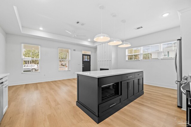 kitchen featuring a tray ceiling, decorative light fixtures, light hardwood / wood-style floors, and a center island