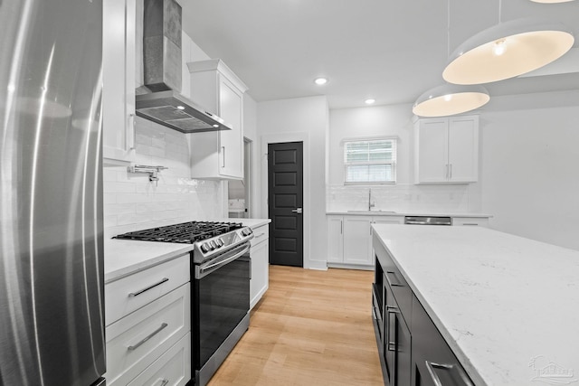 kitchen featuring wall chimney range hood, decorative light fixtures, white cabinets, and appliances with stainless steel finishes