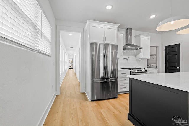 kitchen with wall chimney range hood, appliances with stainless steel finishes, white cabinetry, light stone countertops, and decorative backsplash