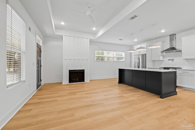 kitchen featuring pendant lighting, wall chimney range hood, stainless steel fridge, white cabinetry, and a center island