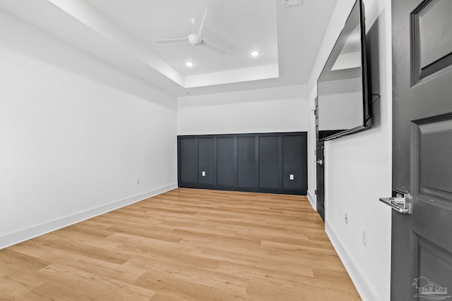 unfurnished bedroom with ceiling fan, a tray ceiling, and light hardwood / wood-style flooring