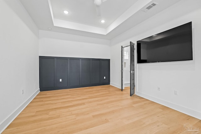 unfurnished bedroom with a tray ceiling and light wood-type flooring