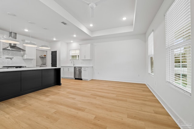 kitchen featuring decorative light fixtures, dishwasher, white cabinets, wall chimney range hood, and light wood-type flooring