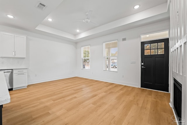 unfurnished living room featuring a raised ceiling, ceiling fan, a large fireplace, and light hardwood / wood-style floors