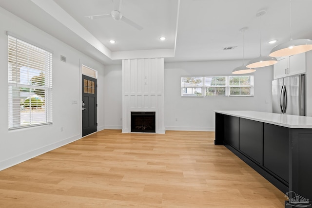 kitchen featuring stainless steel refrigerator, hanging light fixtures, a fireplace, light hardwood / wood-style floors, and white cabinets