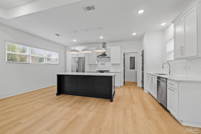 kitchen featuring sink, white cabinetry, pendant lighting, stainless steel appliances, and wall chimney range hood