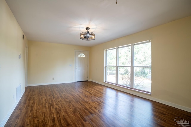 unfurnished room with a notable chandelier and dark wood-type flooring