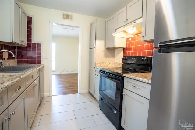 kitchen featuring light stone countertops, sink, stainless steel appliances, light hardwood / wood-style flooring, and backsplash