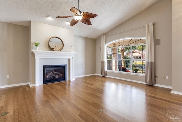 unfurnished living room featuring a ceiling fan, a tiled fireplace, wood finished floors, vaulted ceiling, and a textured ceiling