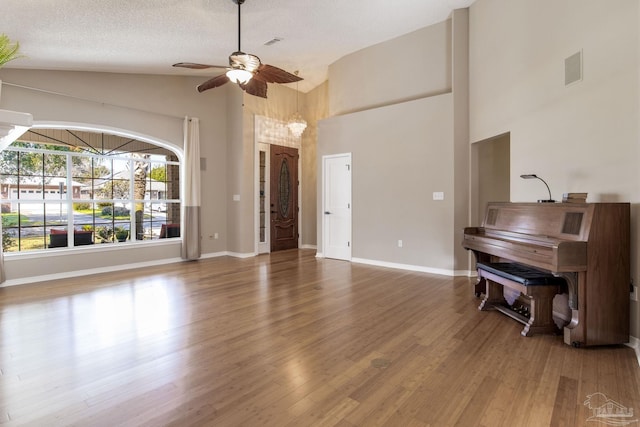 living area with ceiling fan, a textured ceiling, wood finished floors, high vaulted ceiling, and baseboards