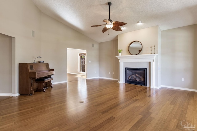 unfurnished living room with baseboards, a ceiling fan, a glass covered fireplace, wood finished floors, and a textured ceiling