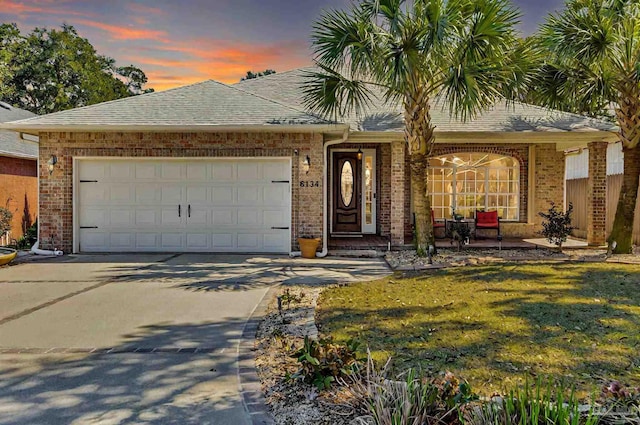 ranch-style home featuring brick siding, a shingled roof, concrete driveway, an attached garage, and a front lawn