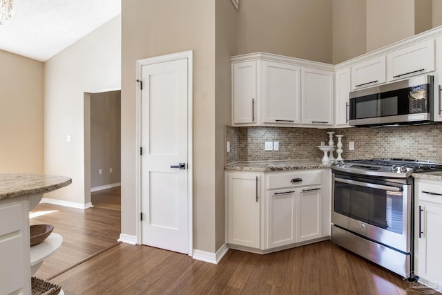 kitchen with backsplash, white cabinetry, stainless steel appliances, and dark wood finished floors