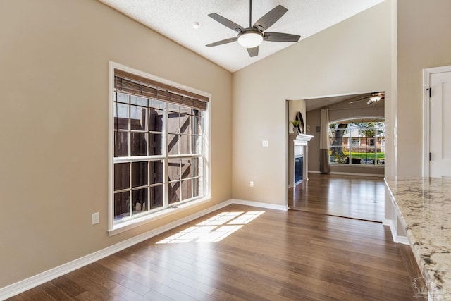 interior space with dark wood-style floors, a glass covered fireplace, lofted ceiling, and baseboards