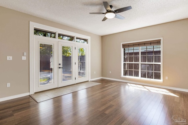 empty room with french doors, a textured ceiling, baseboards, and wood finished floors