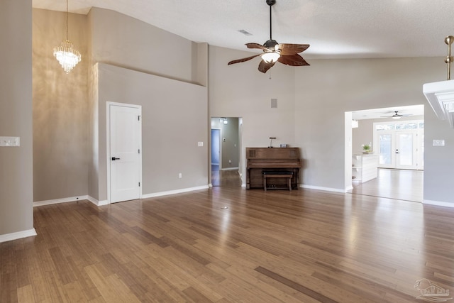 unfurnished living room featuring ceiling fan with notable chandelier, baseboards, and wood finished floors