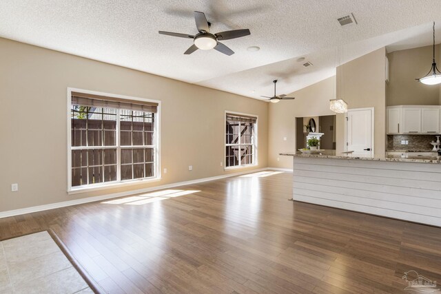 unfurnished living room featuring baseboards, visible vents, a ceiling fan, dark wood-type flooring, and vaulted ceiling