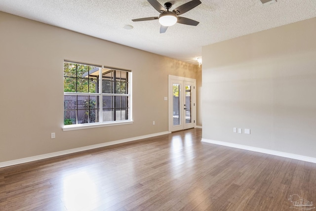 empty room with ceiling fan, a textured ceiling, baseboards, and wood finished floors