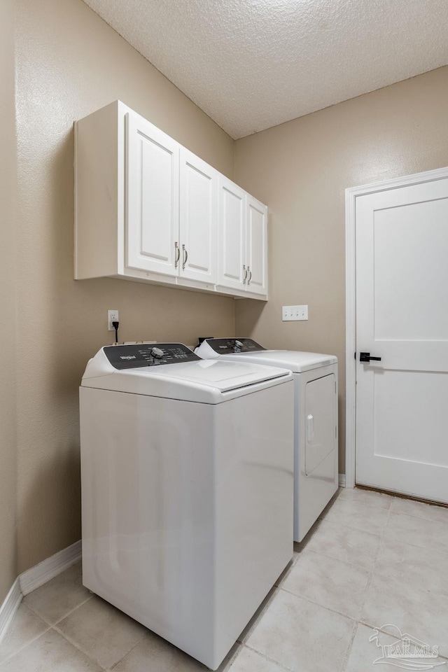 laundry room with a textured ceiling, light tile patterned flooring, baseboards, cabinet space, and washing machine and clothes dryer