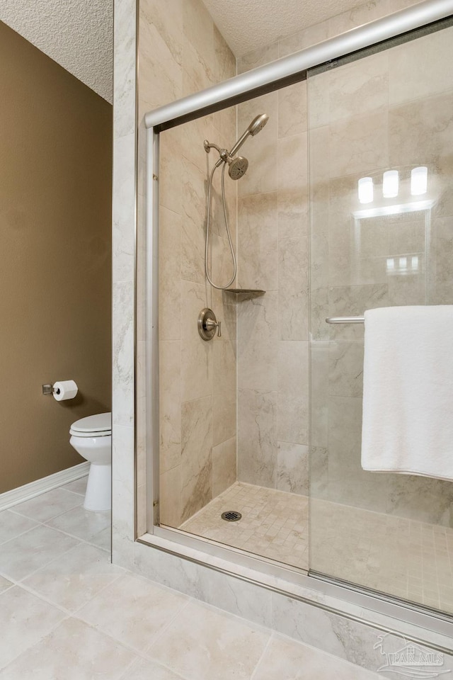 bathroom featuring a textured ceiling, a stall shower, toilet, and tile patterned floors