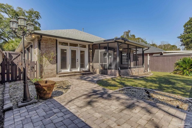 back of property featuring brick siding, fence, a sunroom, a yard, and french doors