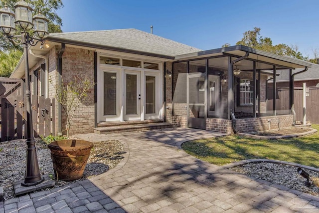 back of house featuring a sunroom, roof with shingles, fence, and brick siding