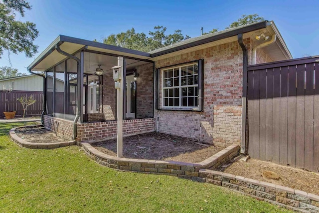 view of property exterior with a yard, a sunroom, brick siding, and fence