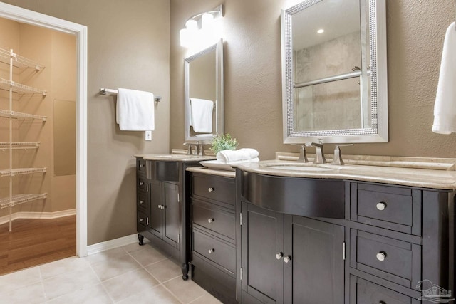 full bath featuring double vanity, a sink, baseboards, and tile patterned floors