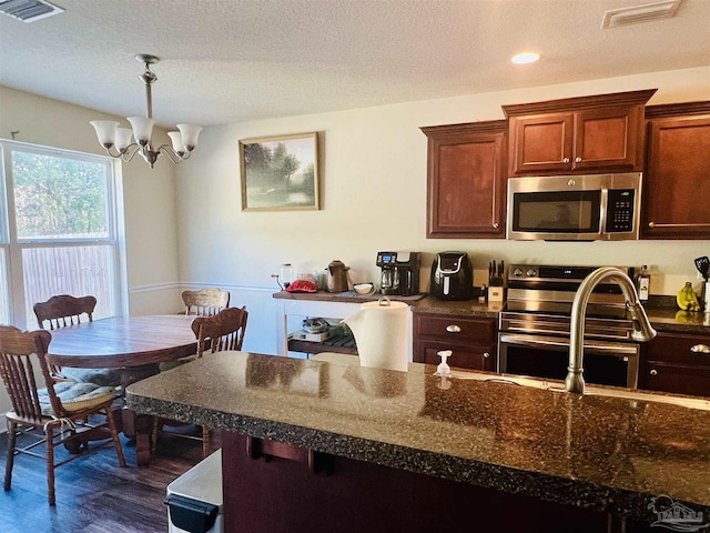 kitchen with appliances with stainless steel finishes, dark stone counters, dark wood-type flooring, decorative light fixtures, and a notable chandelier