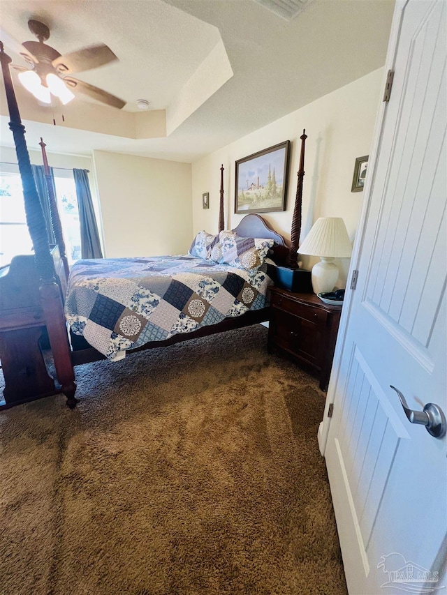 carpeted bedroom featuring ceiling fan and a raised ceiling