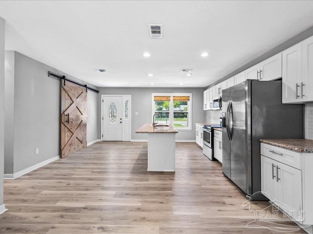 kitchen with an island with sink, light hardwood / wood-style flooring, stone counters, white cabinetry, and stainless steel appliances