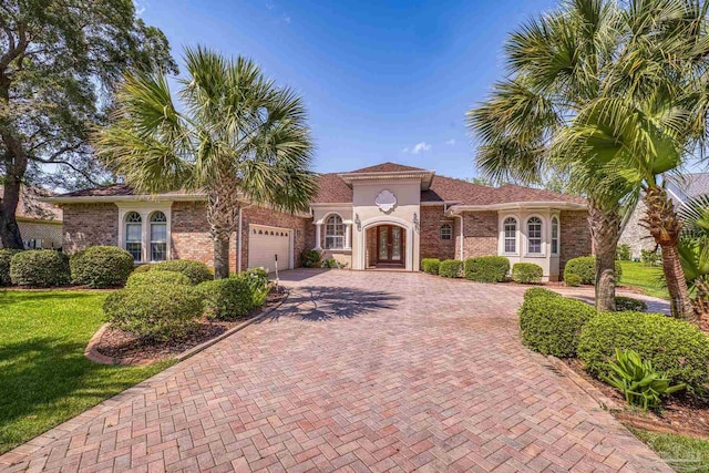 mediterranean / spanish-style house with french doors, a garage, decorative driveway, a front yard, and brick siding
