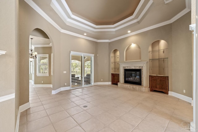 unfurnished living room featuring light tile patterned floors, a tray ceiling, built in features, crown molding, and a fireplace