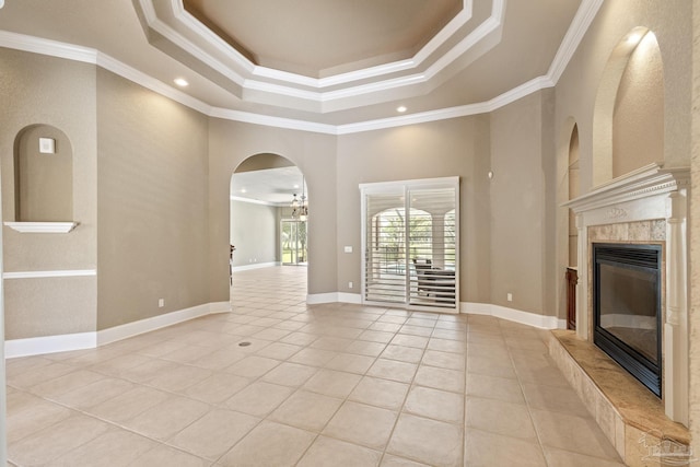 unfurnished living room with a premium fireplace, light tile patterned floors, ornamental molding, a towering ceiling, and a tray ceiling