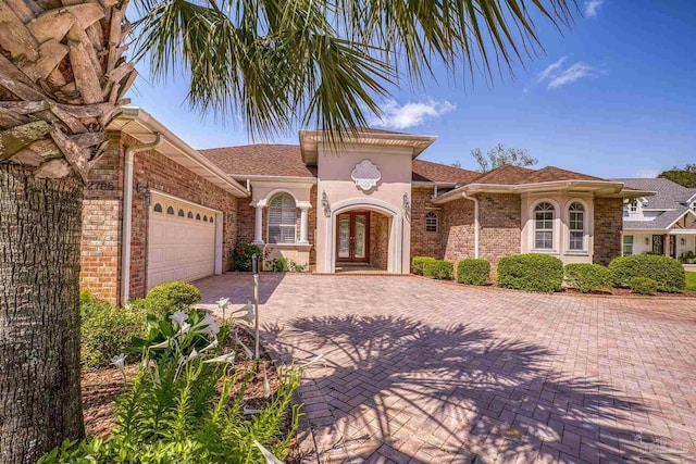 mediterranean / spanish house with french doors, a garage, brick siding, and driveway