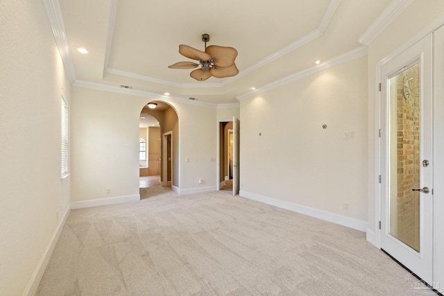 unfurnished room featuring a raised ceiling, arched walkways, light carpet, ornamental molding, and ceiling fan