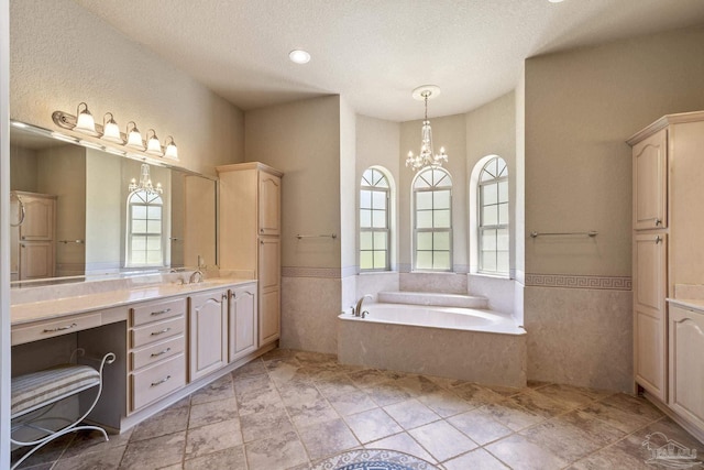 bathroom featuring a textured ceiling, a wainscoted wall, a chandelier, a bath, and vanity