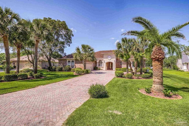 mediterranean / spanish home featuring decorative driveway, a garage, a front yard, and stucco siding