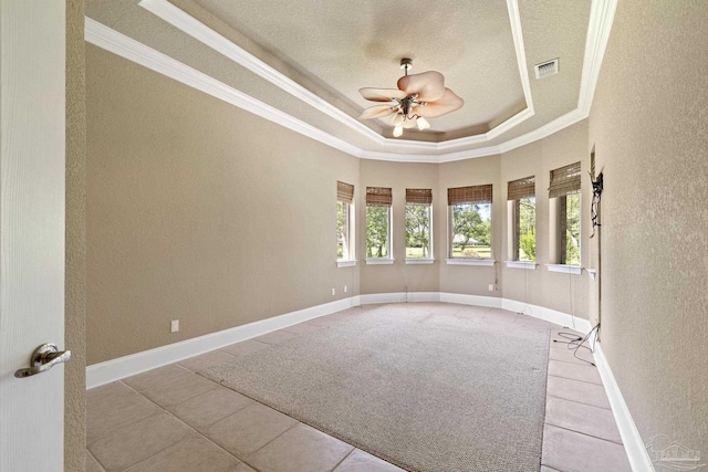 empty room with ornamental molding, a textured wall, a tray ceiling, light tile patterned floors, and ceiling fan