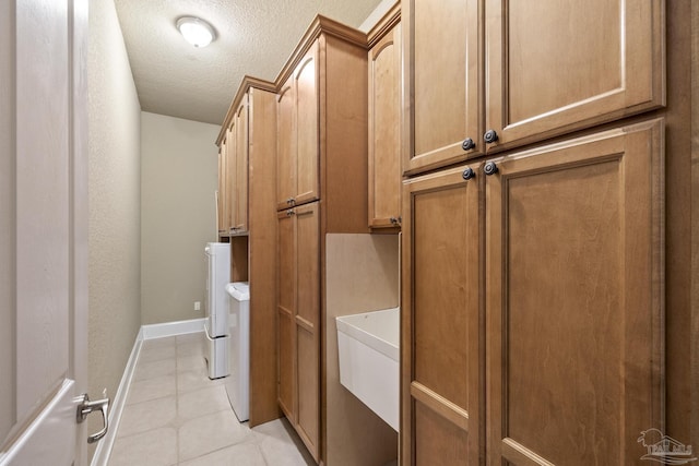 clothes washing area featuring cabinet space, light tile patterned floors, a textured ceiling, washer and clothes dryer, and baseboards